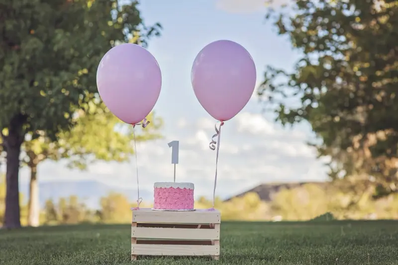 Mesa de aniversário ao ar livre com bolo cor-de-rosa e dois balões